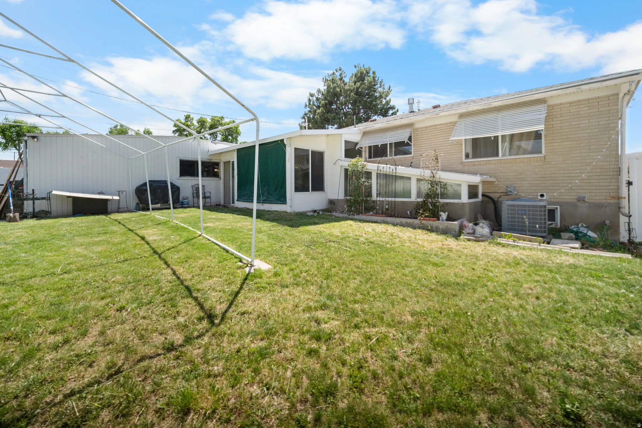 Expansive backyard featuring a large lawn, brick exterior, multiple windows with awnings, and a sunroom with green screening