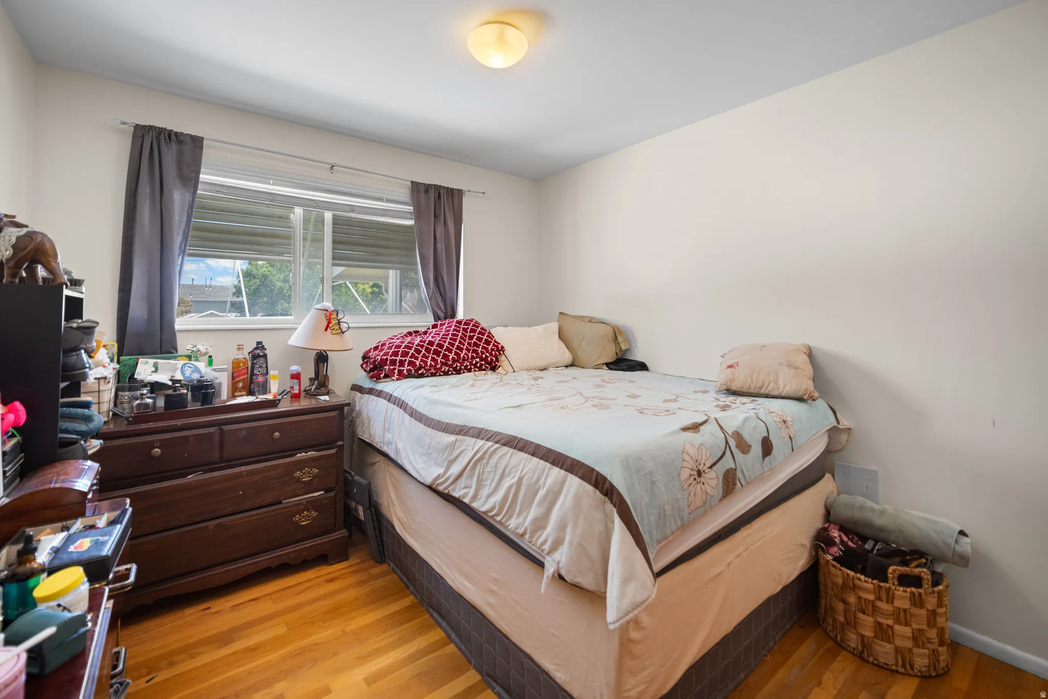 Room with wood-finish flooring and a single window featuring horizontal blinds