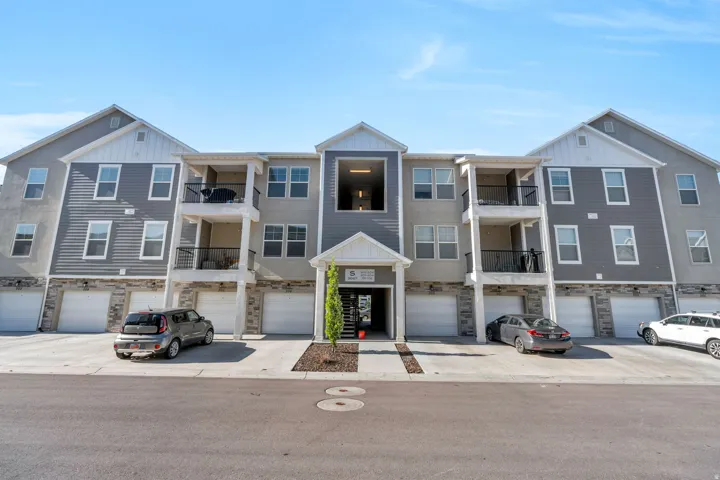 Multi-story residential building featuring gray siding, stone veneer accents, individual garages, and private balconies with black railings