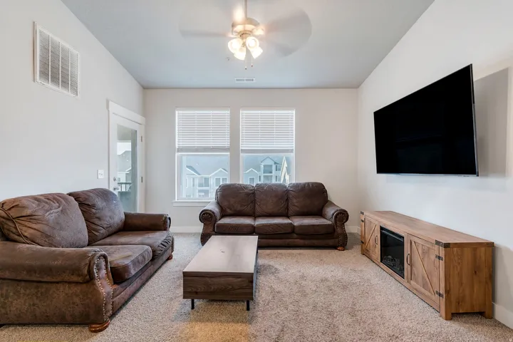 Living area featuring neutral-toned carpet flooring and a ceiling fan with integrated lighting