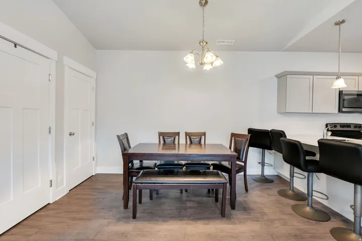 Open-concept dining area featuring wood-finish flooring, a contemporary chandelier, and a breakfast bar with pendant lighting