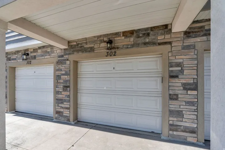 Attached garages featuring white paneled doors, stone veneer accents, and concrete driveways