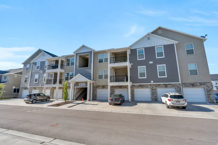 Contemporary multi-level building featuring varied siding, stone veneer accents, individual garage doors, multiple balconies with dark railings, and prominent gabled roofs