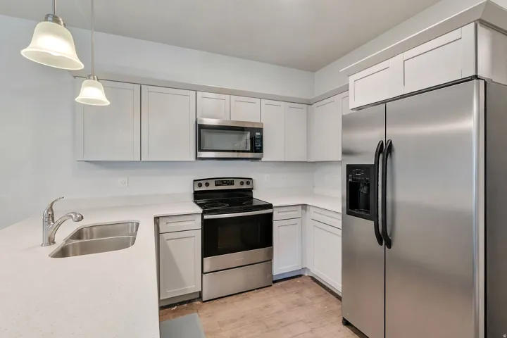 Modern kitchen featuring white shaker cabinetry, stainless steel appliances, light countertops, and wood-finish flooring