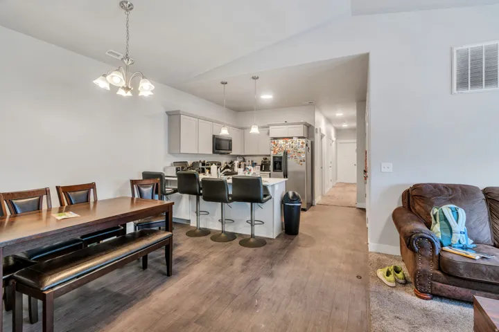 Open-concept living area featuring wood-finish flooring, a contemporary kitchen island with seating, pendant lighting, stainless steel appliances, and light gray cabinetry