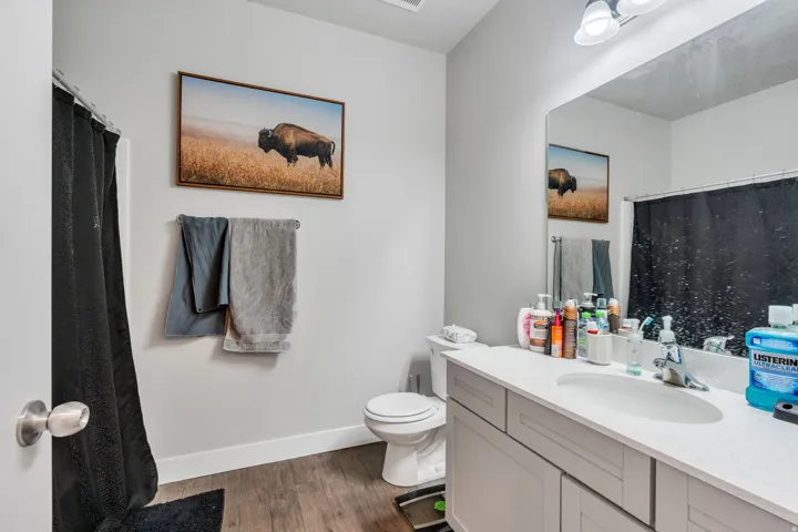 Bathroom featuring a single vanity with an integrated sink, a large wall-mounted mirror, and wood-finish flooring