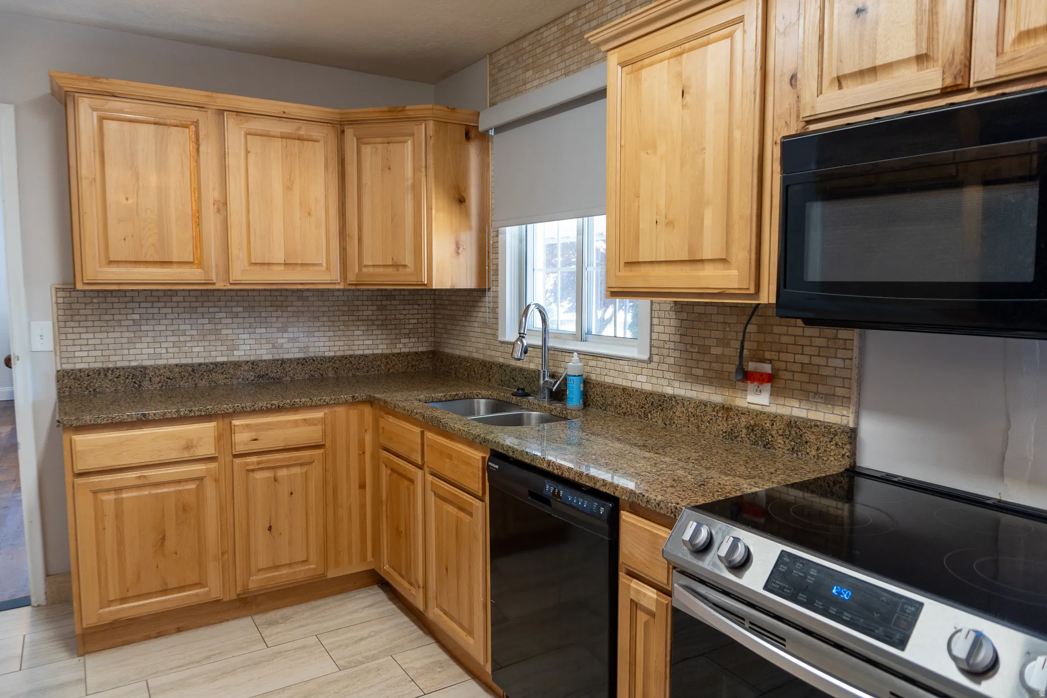 Kitchen featuring light wood cabinetry, stone countertops, a tile backsplash, stainless steel sink with a gooseneck faucet, and a black built-in microwave