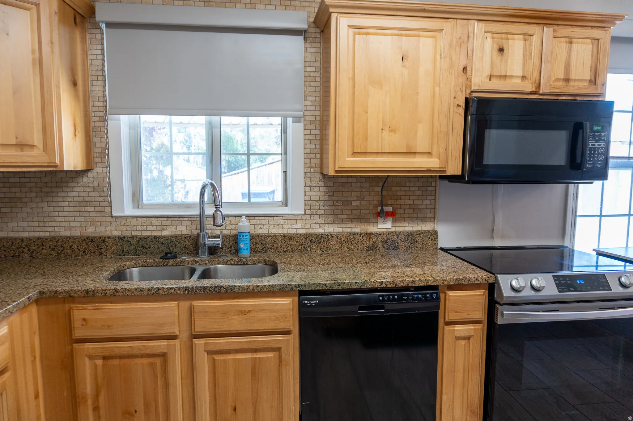 Kitchen featuring natural wood cabinetry, light-toned mosaic tile backsplash, double basin stainless steel sink, and stainless steel appliances