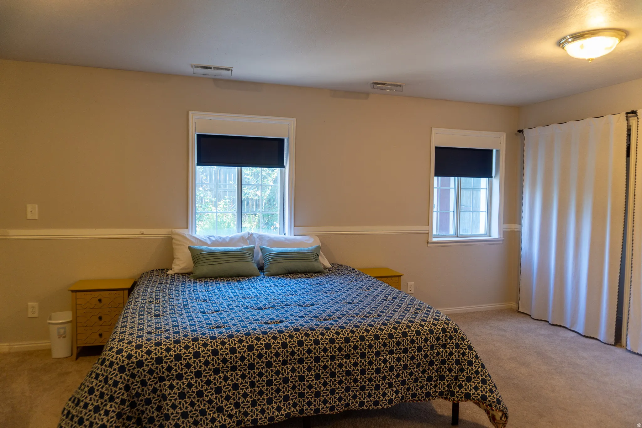 Carpeted room with two windows featuring dark roller shades, a light fixture, and white wall paneling