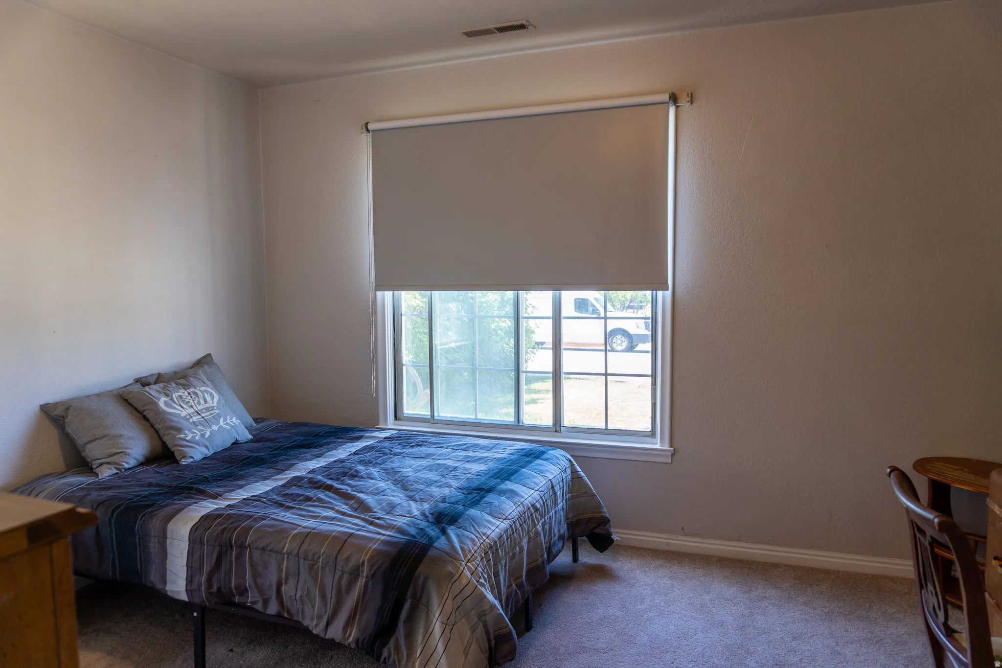 Room featuring a window with a roller shade, light-colored walls, and carpeting