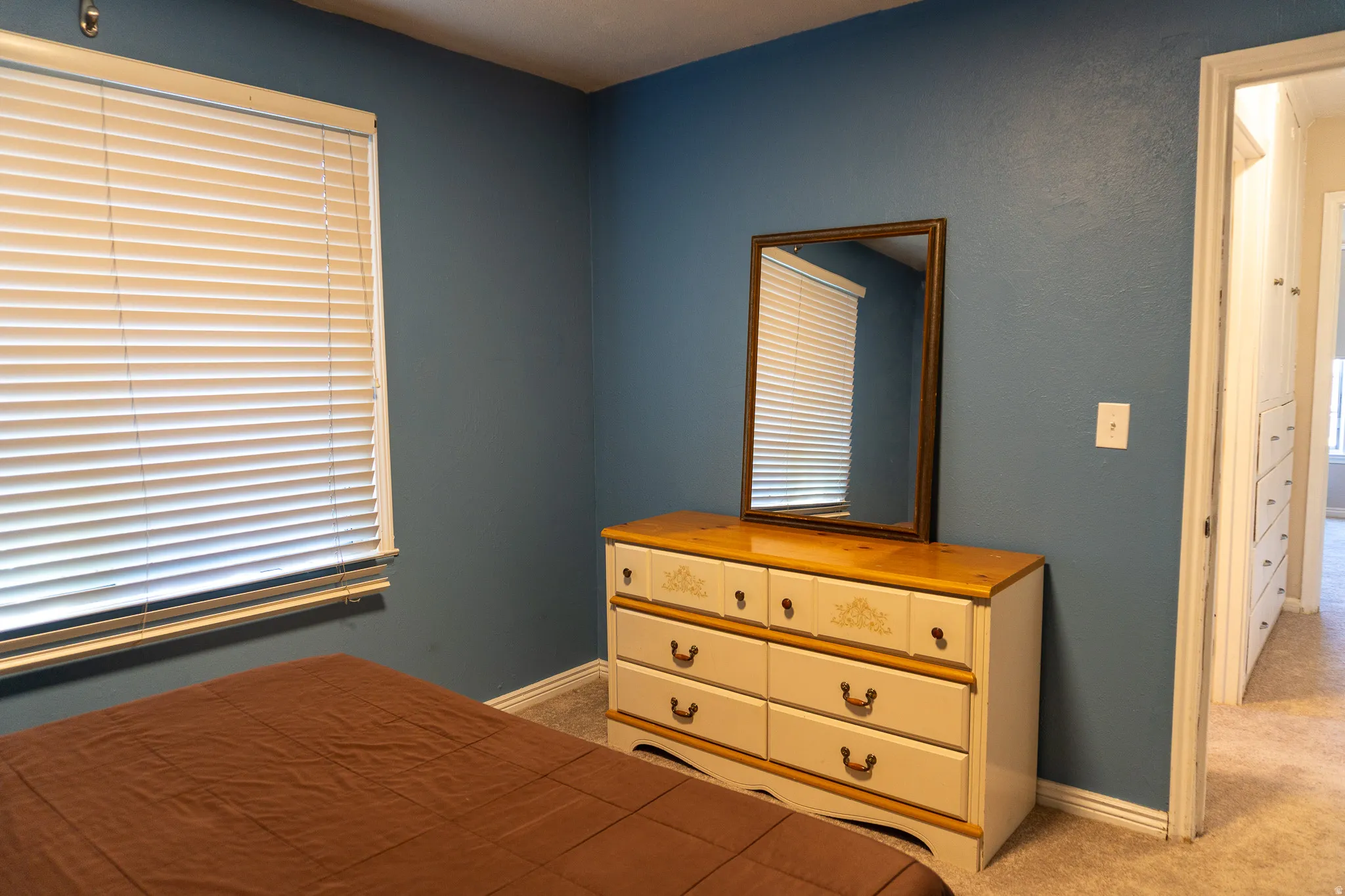 Bedroom featuring a window with white blinds, blue painted walls, and light-toned carpeting