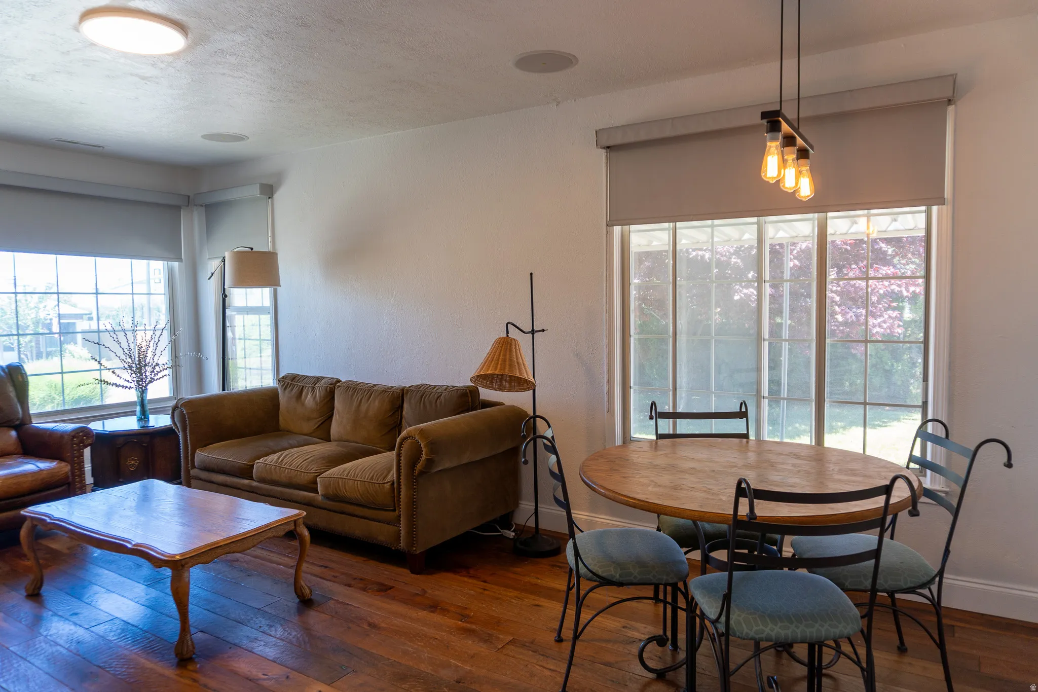 Spacious room featuring wood-finish flooring, multiple windows, a modern pendant light fixture, and recessed ceiling lighting