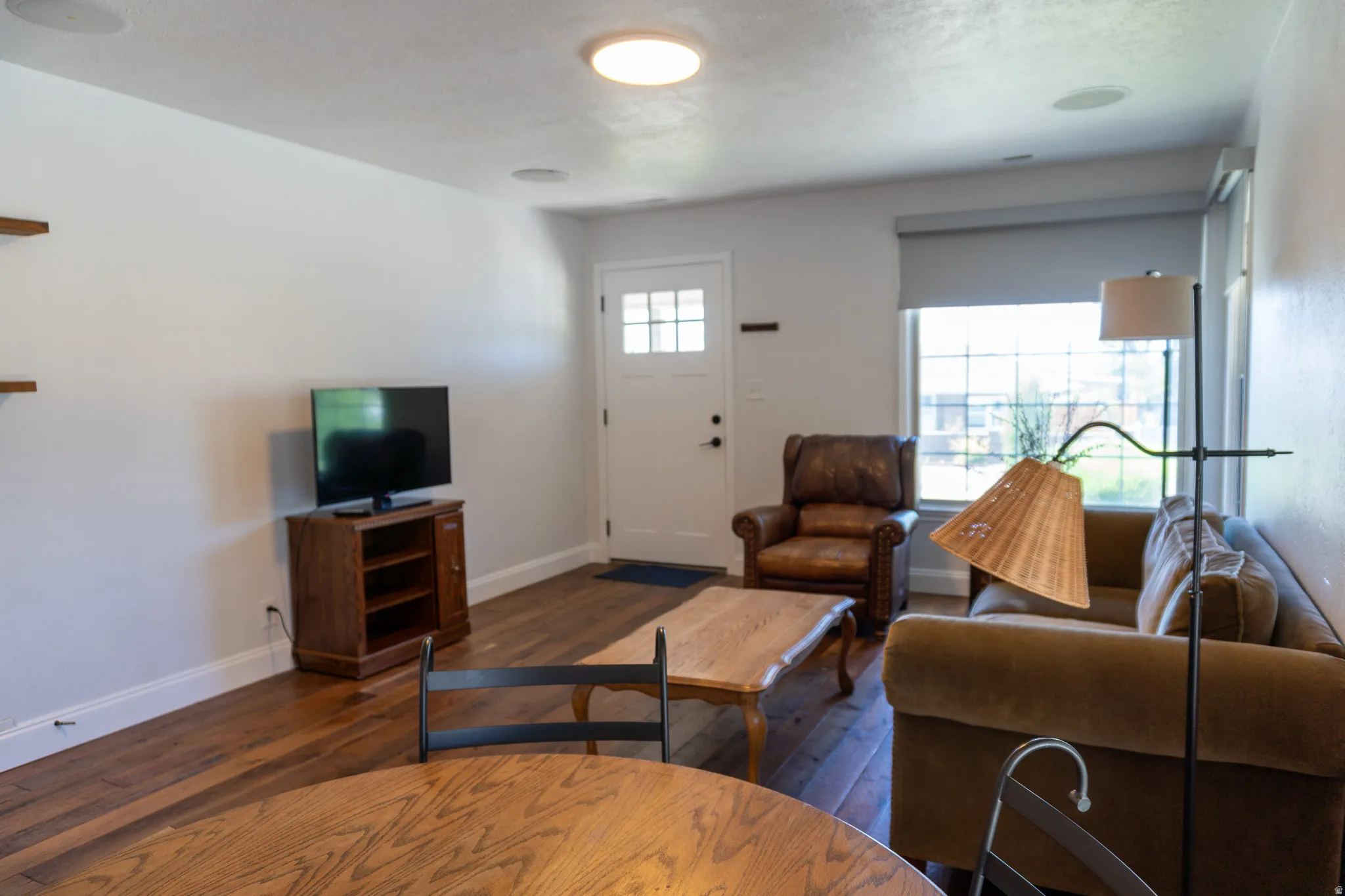 Bright living area featuring wood-finish flooring, white baseboards, and a white entry door with glass panes