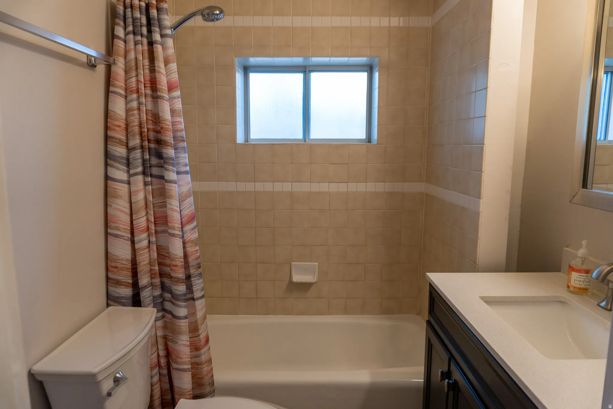 Bathroom featuring a tub/shower combination with beige tile surround, a frosted window, and a dark wood-finish vanity with an integrated sink