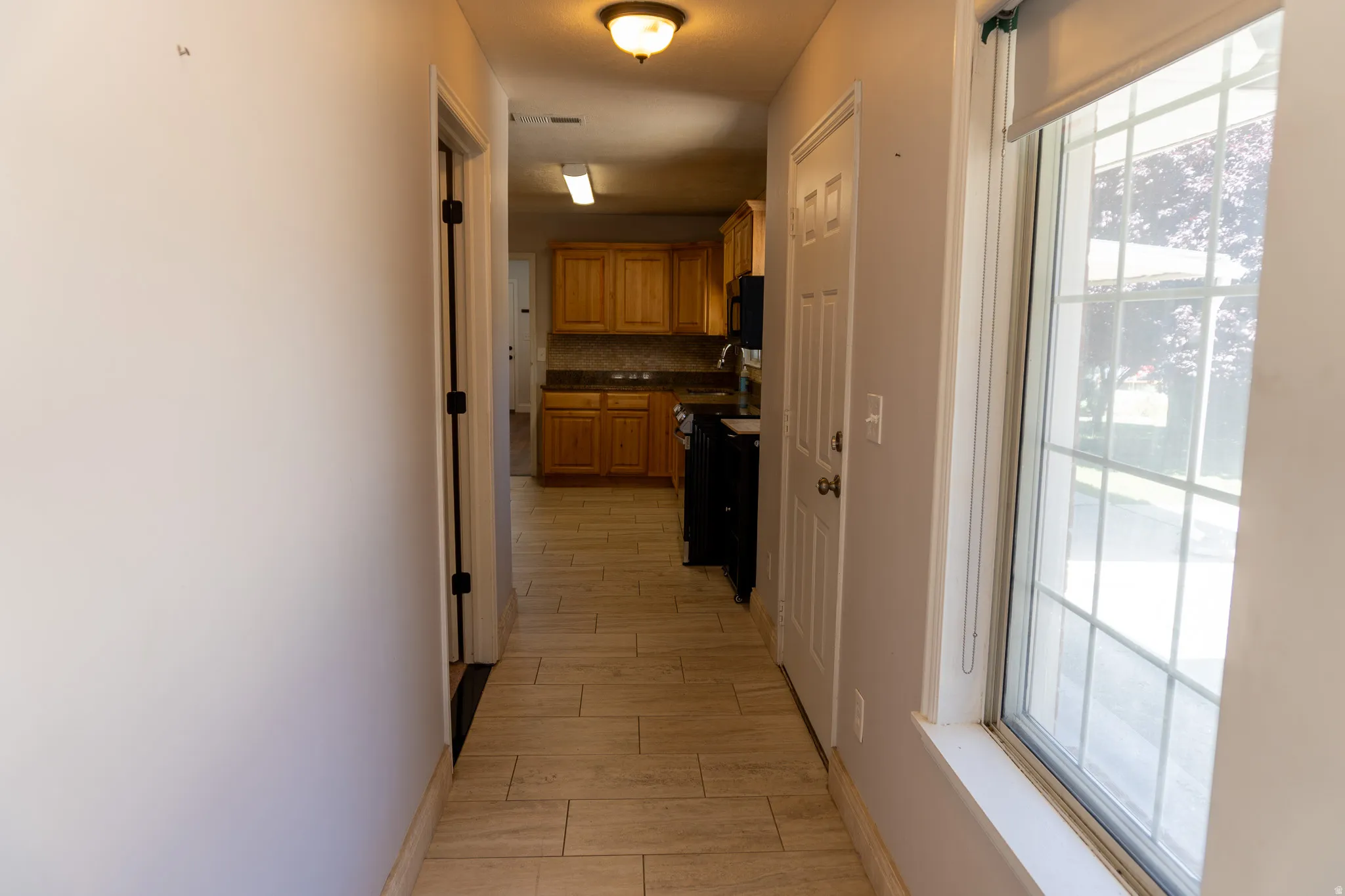 Hallway with tile flooring, featuring a window with grid pattern, and a kitchen with wood cabinetry and dark countertops