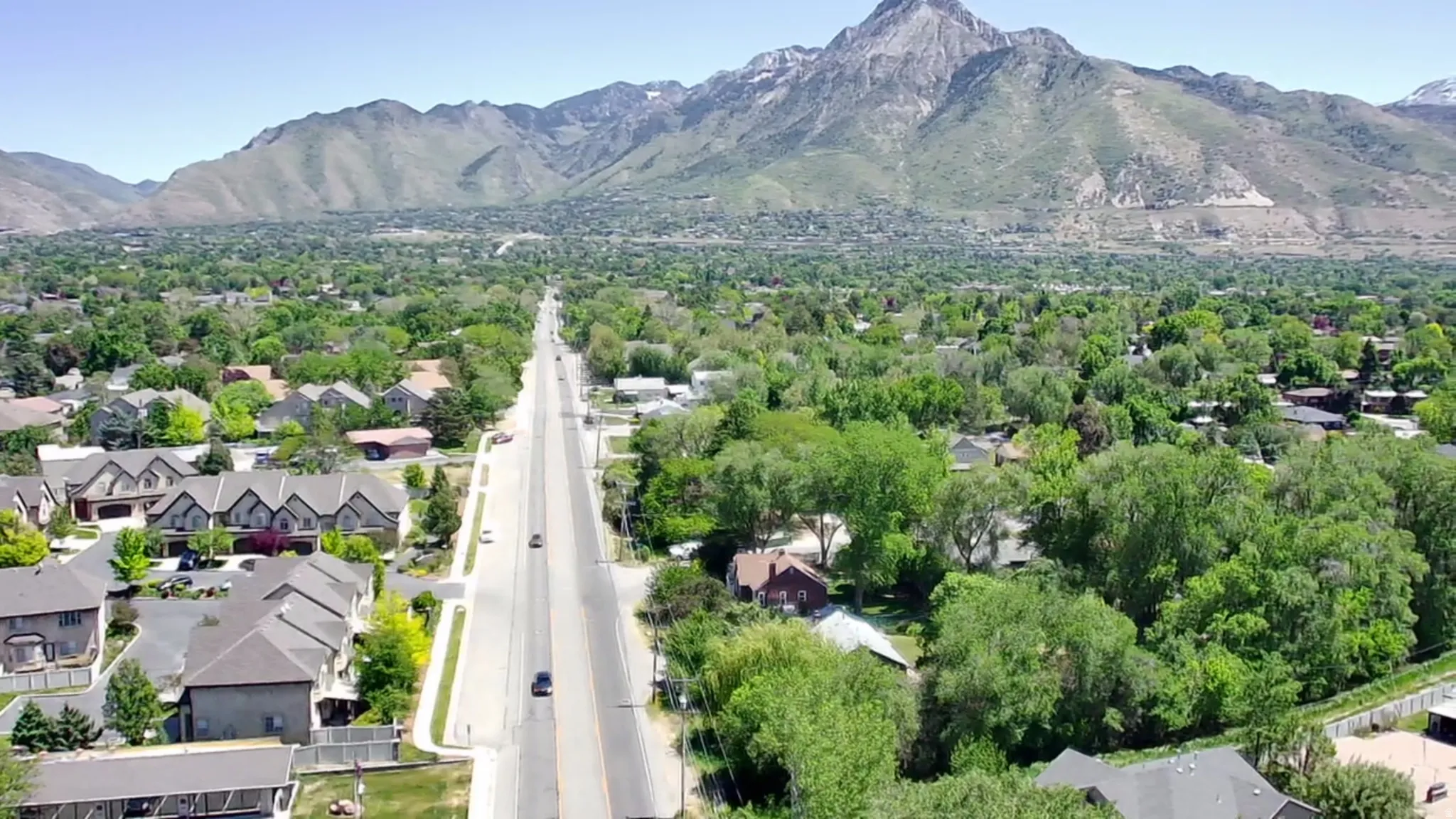 Expansive urban landscape featuring a prominent roadway, extensive green tree canopy, and distant mountains