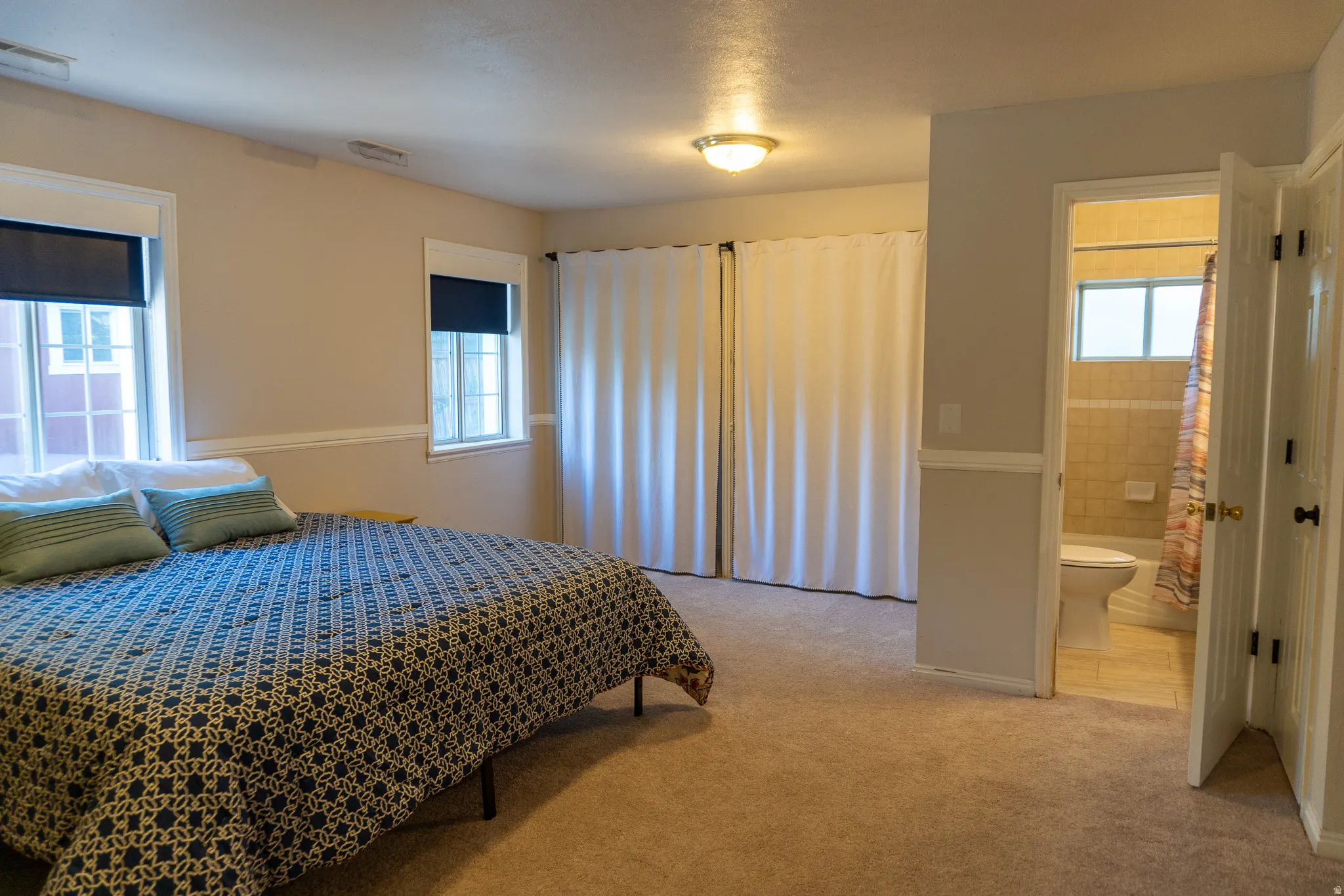 Carpeted room featuring two windows with roller shades, a ceiling-mounted light fixture, and two sets of bifold closet doors