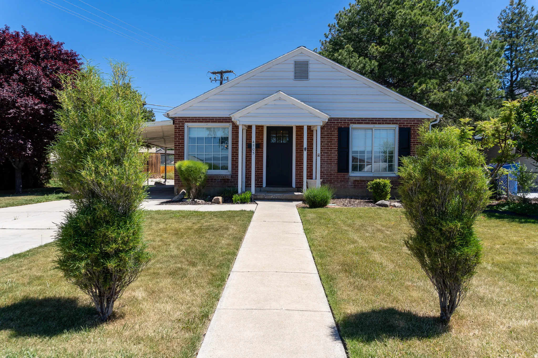 Brick-front residence featuring white siding, a covered entry with columns, a dark entry door, and a concrete walkway