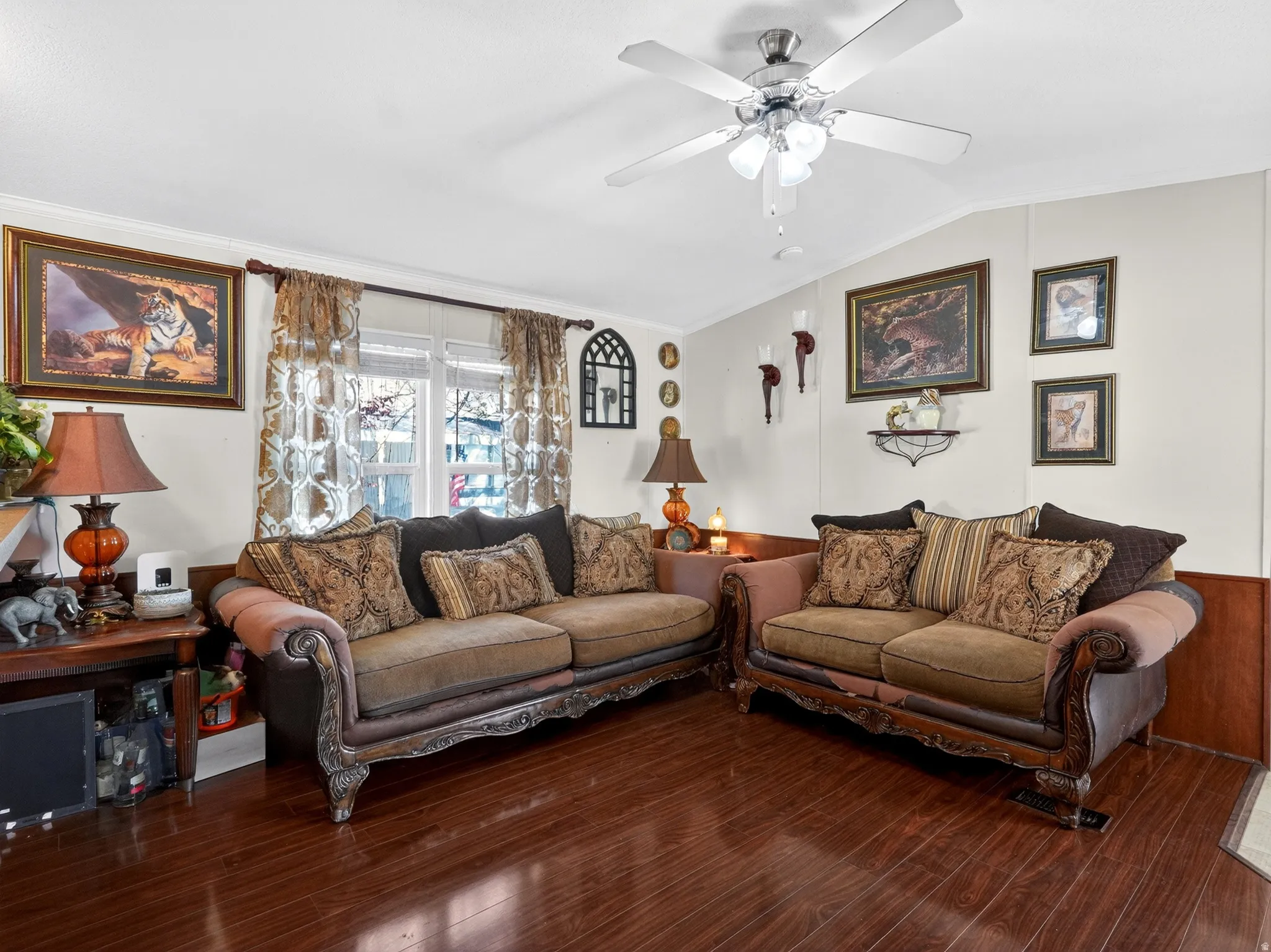 Living area featuring wood-finish flooring, white walls with wood wainscoting, a ceiling fan with integrated lighting, and a double window with blinds