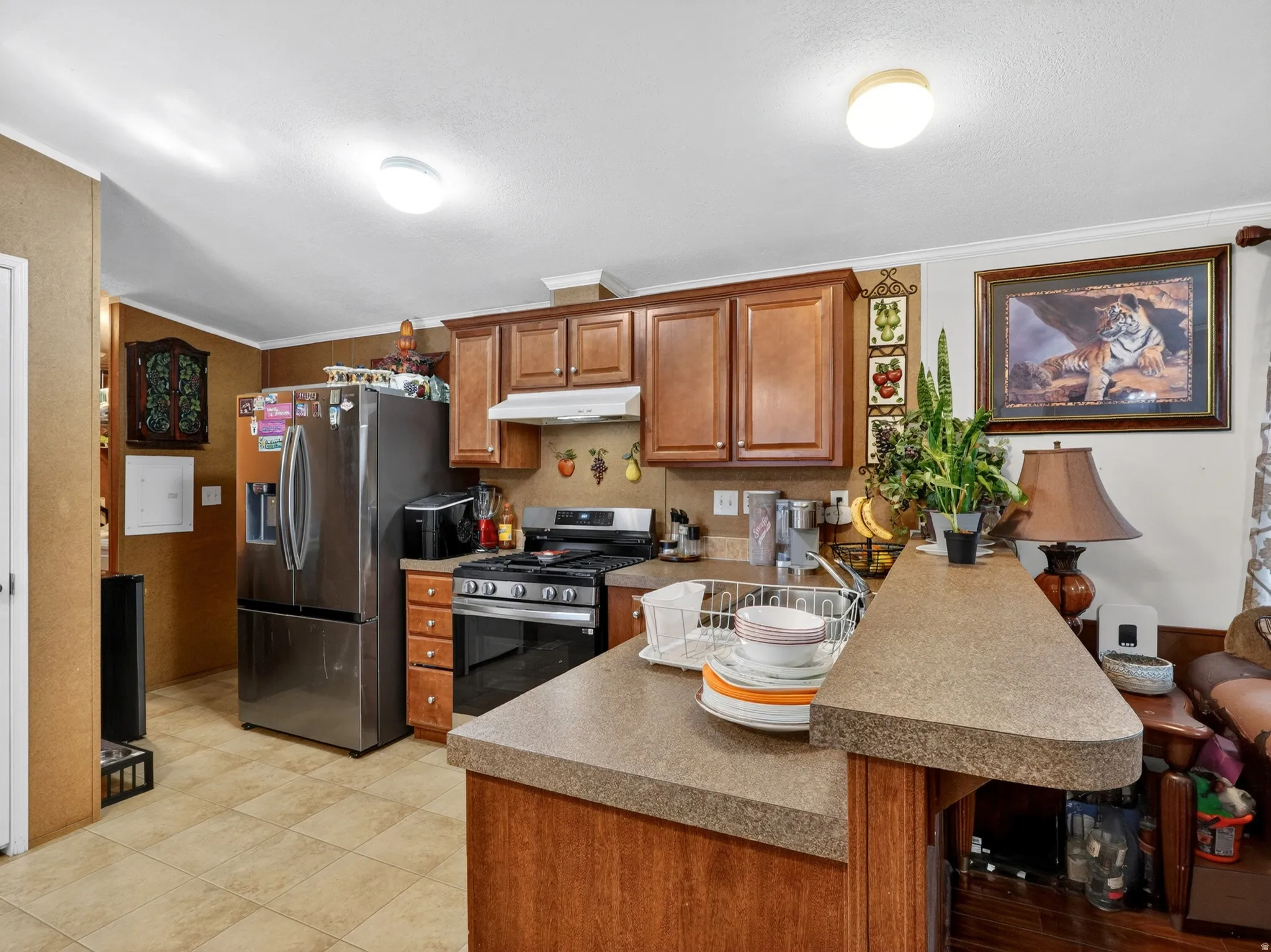 Kitchen featuring wood cabinetry, a stainless steel refrigerator, and a gas range with an overhead vent