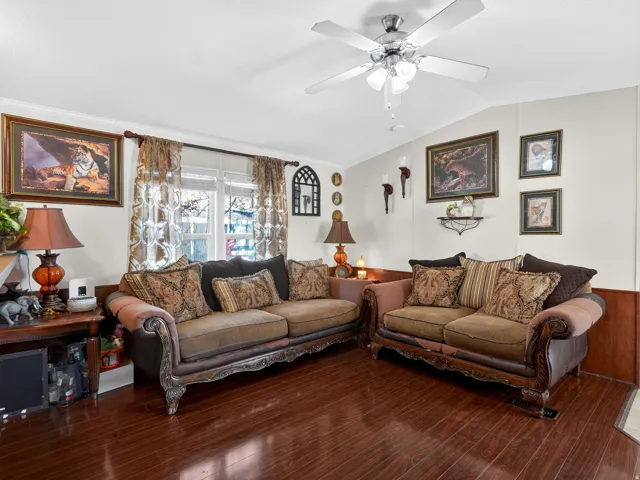 Living area featuring wood-finish flooring, white walls with wood wainscoting, a ceiling fan with integrated lighting, and a double window with blinds