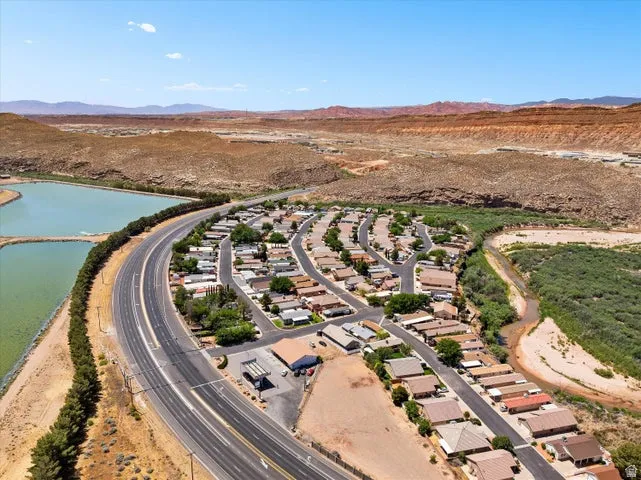 Residential development situated among desert terrain, featuring a curved roadway, two bodies of water, and a natural waterway bordered by green vegetation
