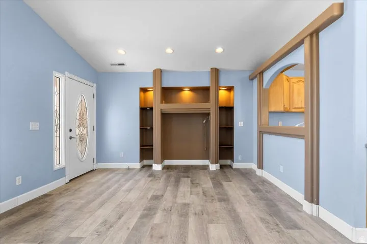 Open living area featuring wood-finish flooring, recessed lighting, and a decorative front entry door with an oval glass insert