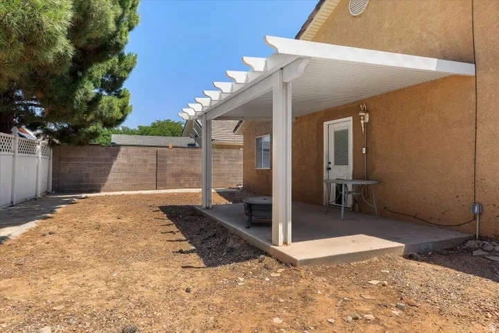 Expansive backyard featuring a concrete patio with a white pergola, textured exterior wall, white lattice fencing, and a block perimeter wall