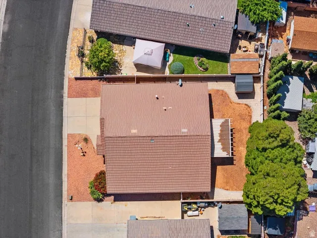 Aerial view showcasing a property with a brown shingle roof, concrete driveway, and a combination of landscaped and natural ground cover