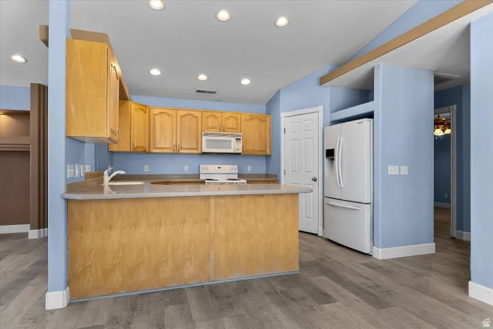 Kitchen featuring light wood cabinetry, a two-tier island with a sink, a white built-in microwave, and a white electric range