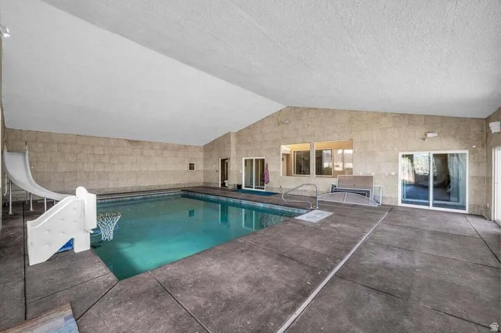Indoor swimming pool with concrete decking, a white slide, and multiple sliding glass doors