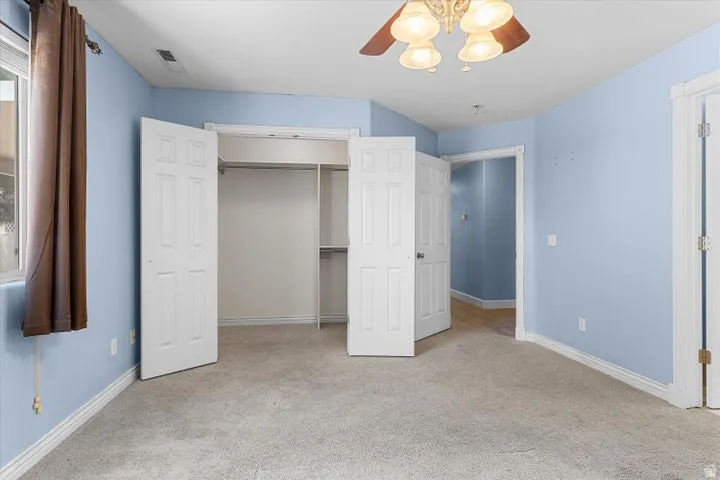 Carpeted interior room featuring light blue walls, a multi-pane window, and a ceiling fan with integrated lighting