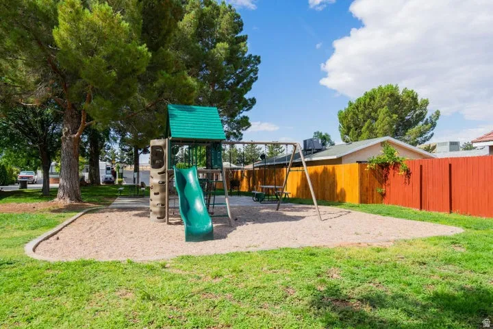 Outdoor play area featuring a green slide, climbing wall, and swing set