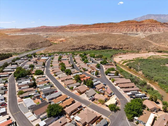 Residential community with winding streets and varied home styles, bordered by a natural waterway and desert landscape featuring red rock formations