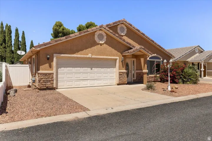 Stucco exterior featuring a two-car garage, stone accents, and a covered entry