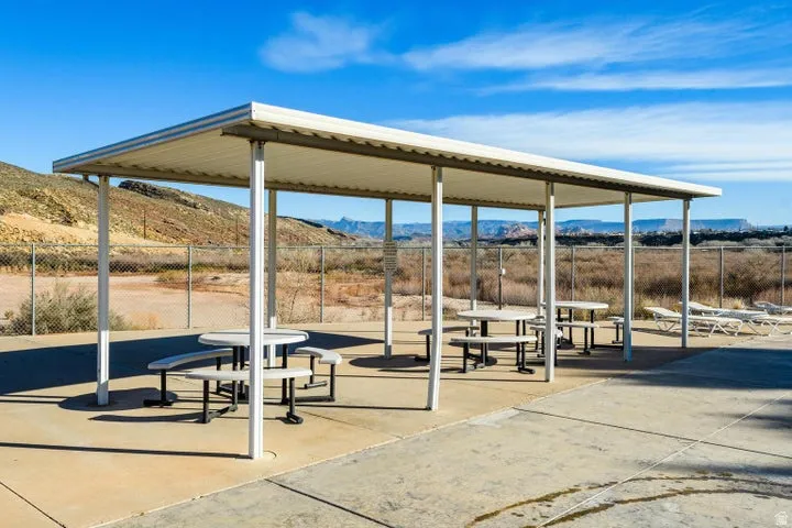 Covered outdoor patio area featuring a metal roof structure, multiple picnic tables, and a concrete paver surface