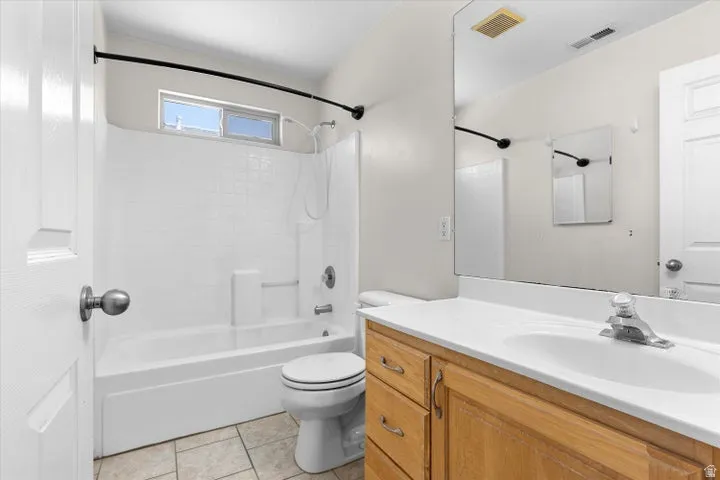 Bathroom featuring a tub/shower combination with white subway tile surround, a single vanity with wood-finish cabinetry, a white countertop, and tiled flooring