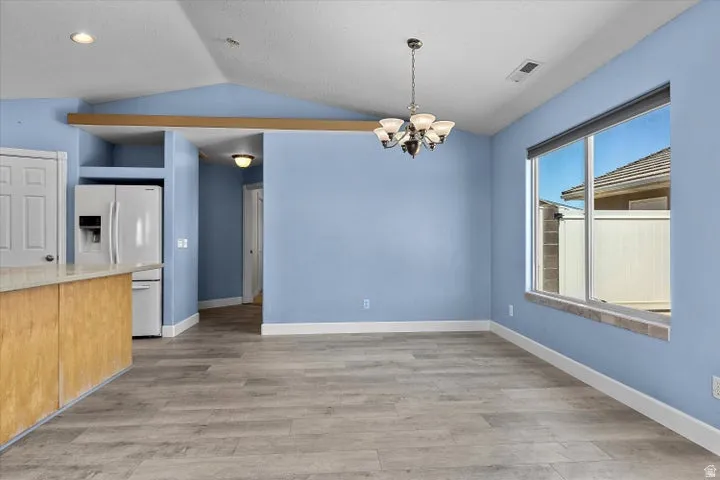 Vaulted ceiling room featuring wood-finish flooring, a chandelier, and a large window with a tile sill