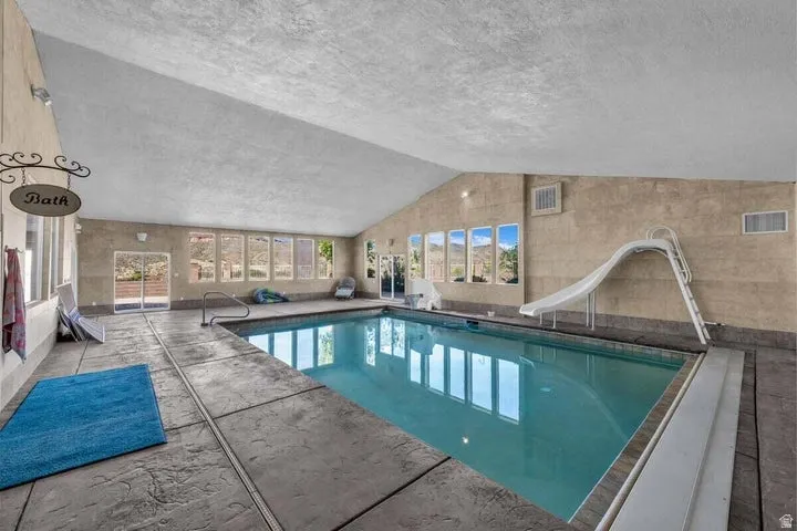 Indoor swimming pool featuring a water slide, multiple windows, a sloped ceiling, and textured concrete flooring