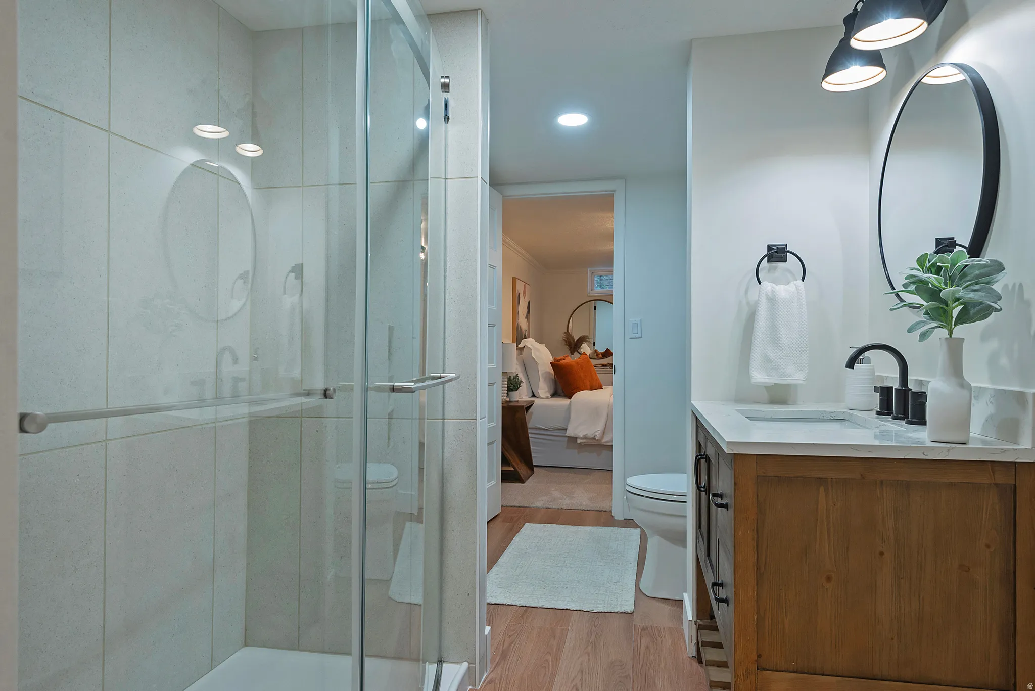 Bathroom featuring a glass-enclosed shower with light-toned wall tile, a wood-finish vanity with a light-colored countertop, a black framed mirror, and matte black plumbing fixtures