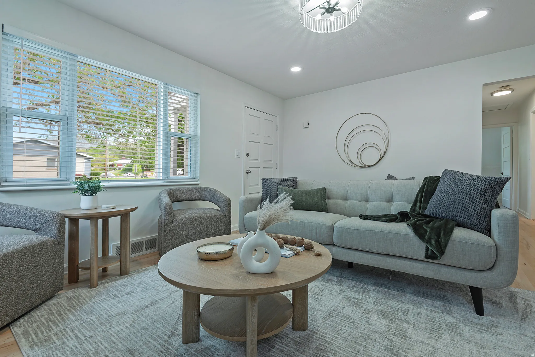 Bright living area featuring wood-finish flooring, recessed lighting, a decorative ceiling fixture, and a large window with horizontal blinds