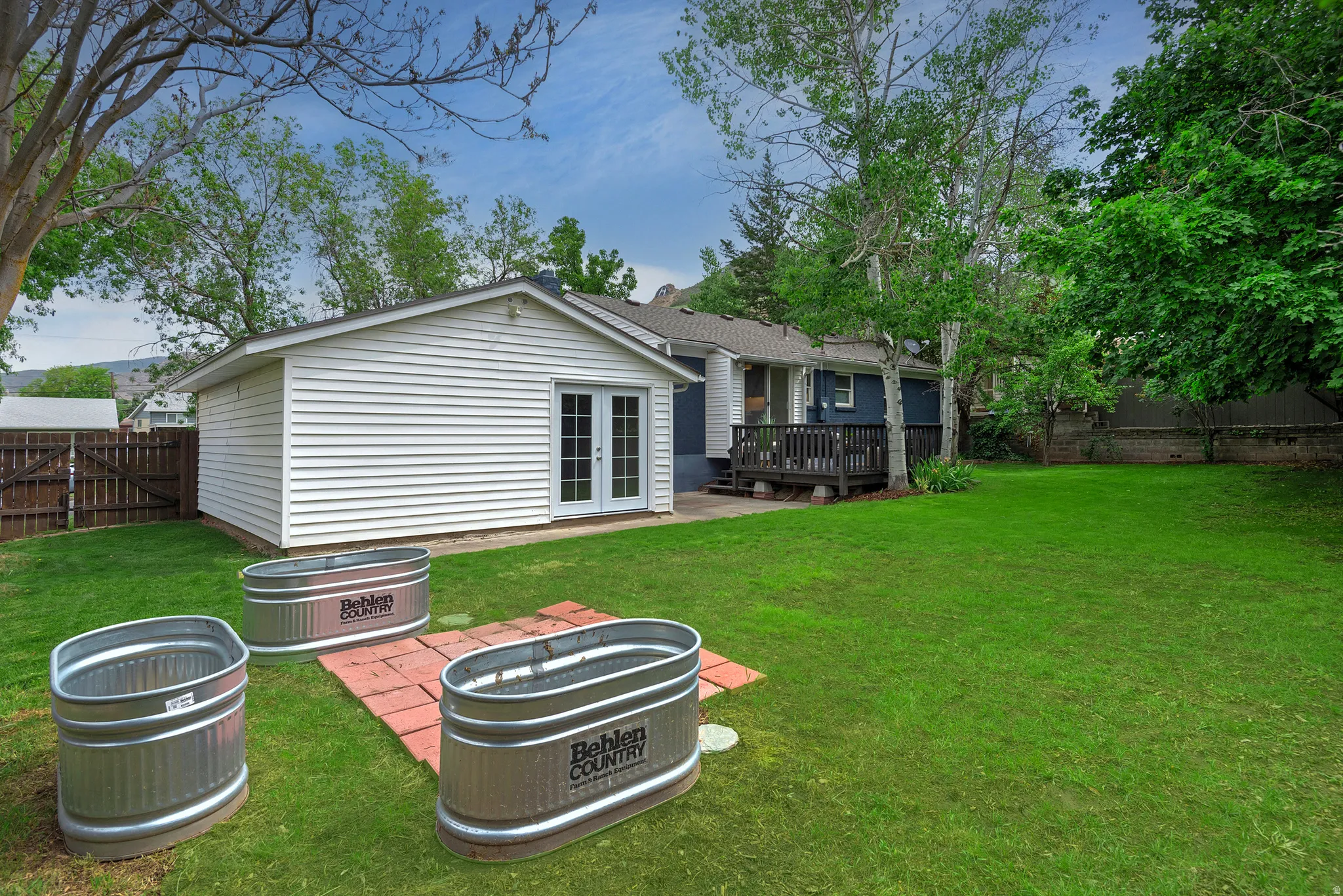 Expansive backyard featuring a detached outbuilding with white siding and glass French doors, a dark wood deck, a wood privacy fence, and mature trees