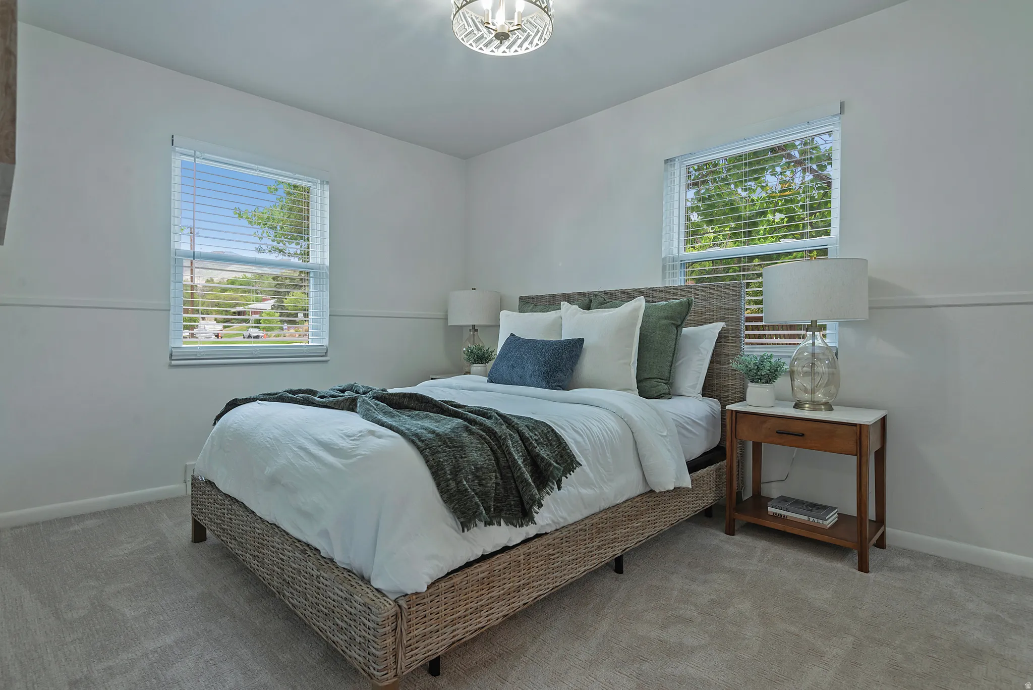 Light gray carpeted bedroom featuring white walls, two windows with blinds, and a decorative ceiling light fixture