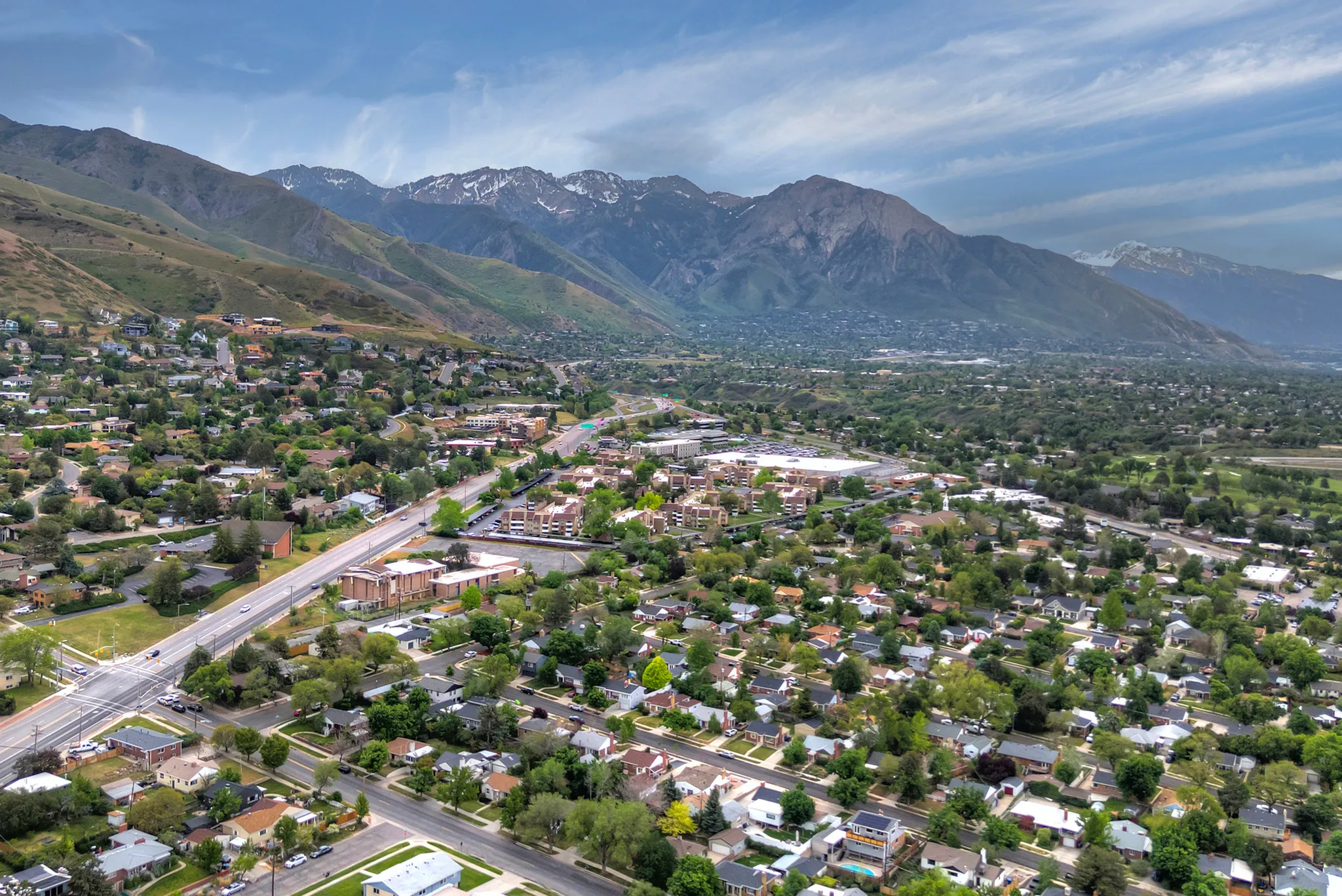 Expansive aerial perspective showcasing a residential area with lush green trees, set against a backdrop of majestic mountains