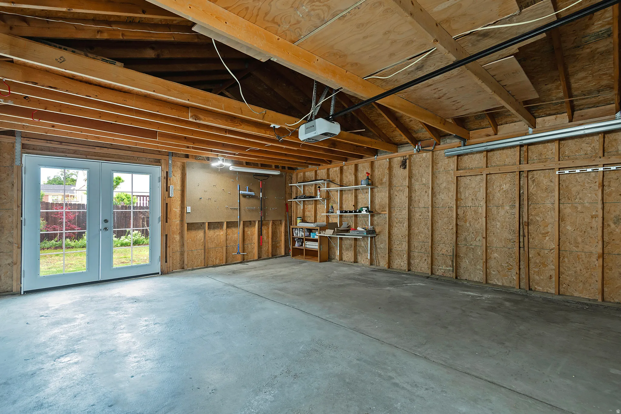 Spacious garage featuring a concrete floor, exposed wood ceiling joists, and a double French door leading to a backyard