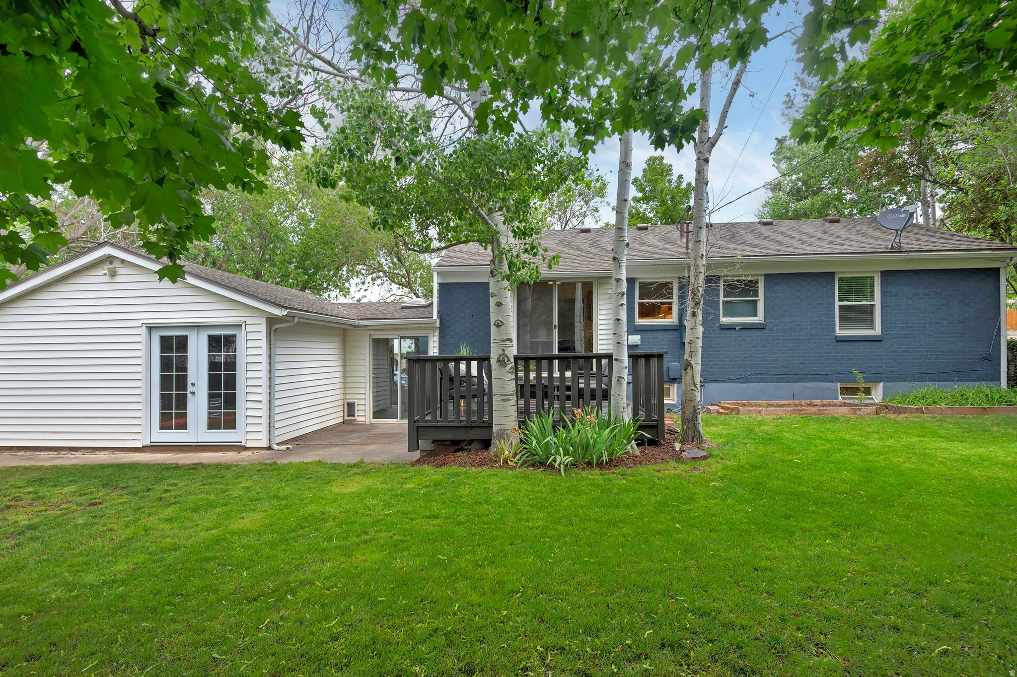 Expansive backyard featuring a lush lawn, established trees, a concrete patio, and a wood deck