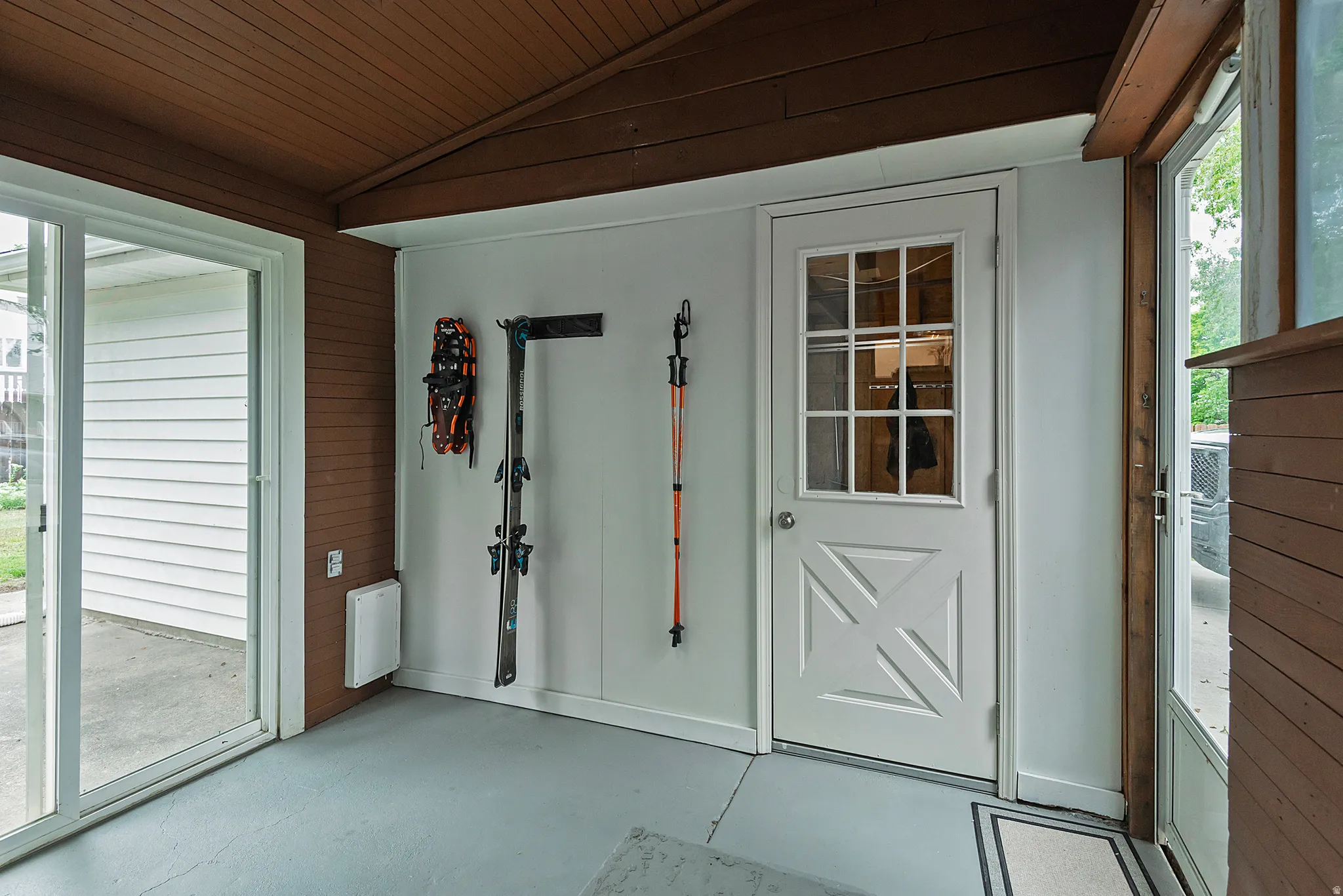 Enclosed patio featuring a sliding glass door, white paneled door with windowpanes, light gray flooring, and a warm brown wood-paneled ceiling