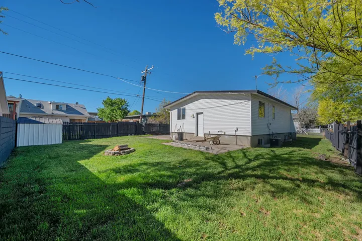 Spacious backyard featuring a manicured lawn, full perimeter fencing, and a stone-lined fire pit