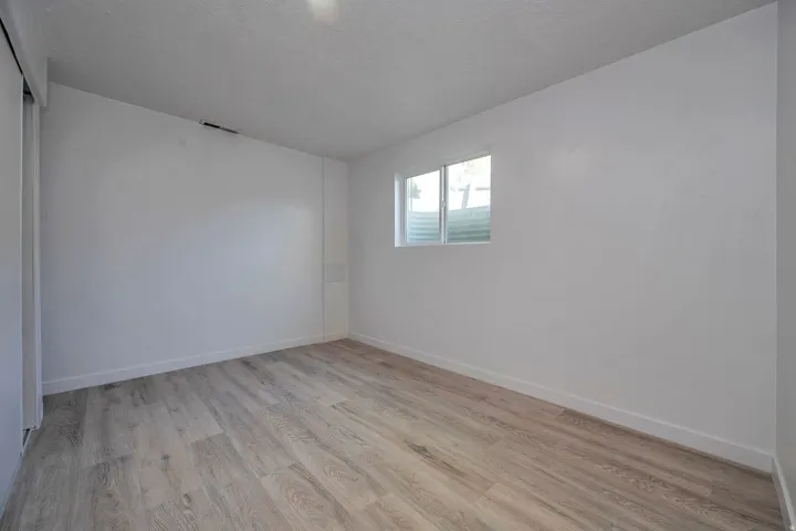 Spacious room featuring light wood-finish flooring, white walls, and a window with a window well