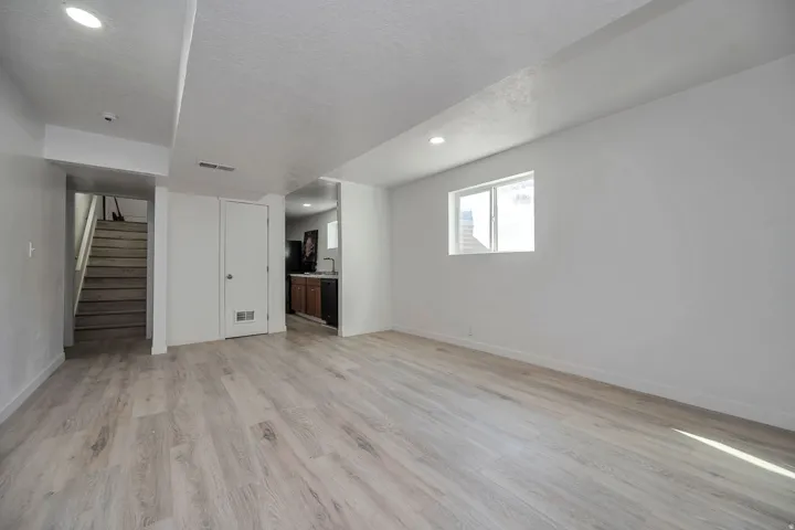 Spacious room featuring light wood-finish flooring, recessed lighting, a window with horizontal blinds, and fresh white walls